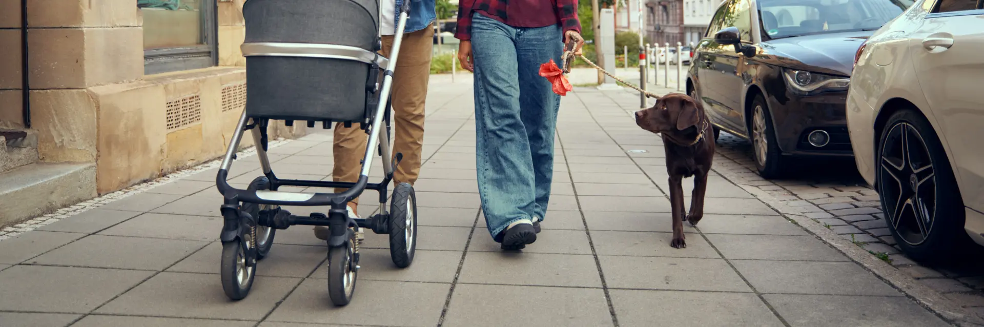 Familie mit Kinderwagen und Hund auf einem Gehweg